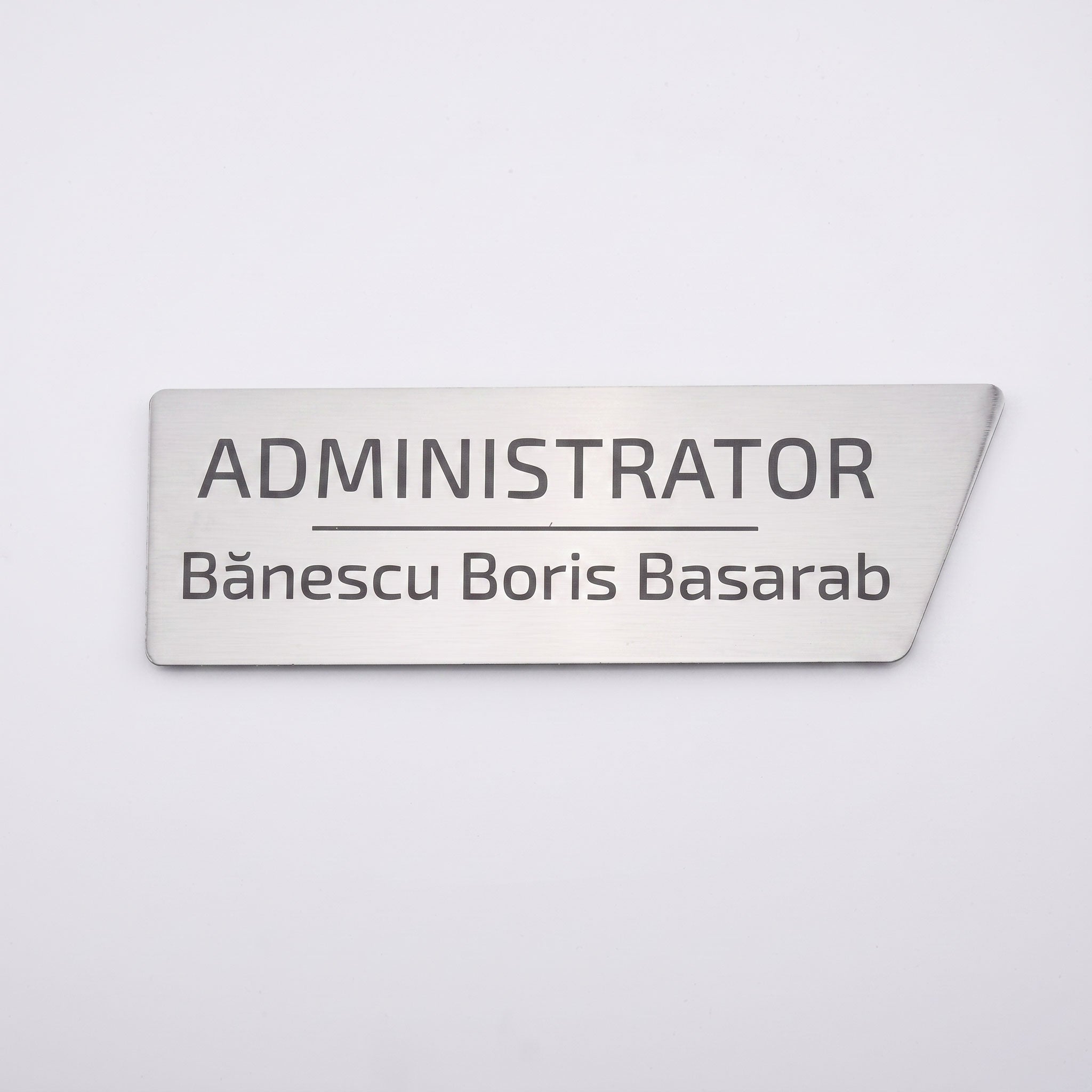 Plăcuță de identificare simplă pentru birou din metal argintiu periat, cu tăietură asimetrică pe colțul din dreapta, gravată cu textul „ADMINISTRATOR Bănescu Boris Basarab”, pe fundal alb.