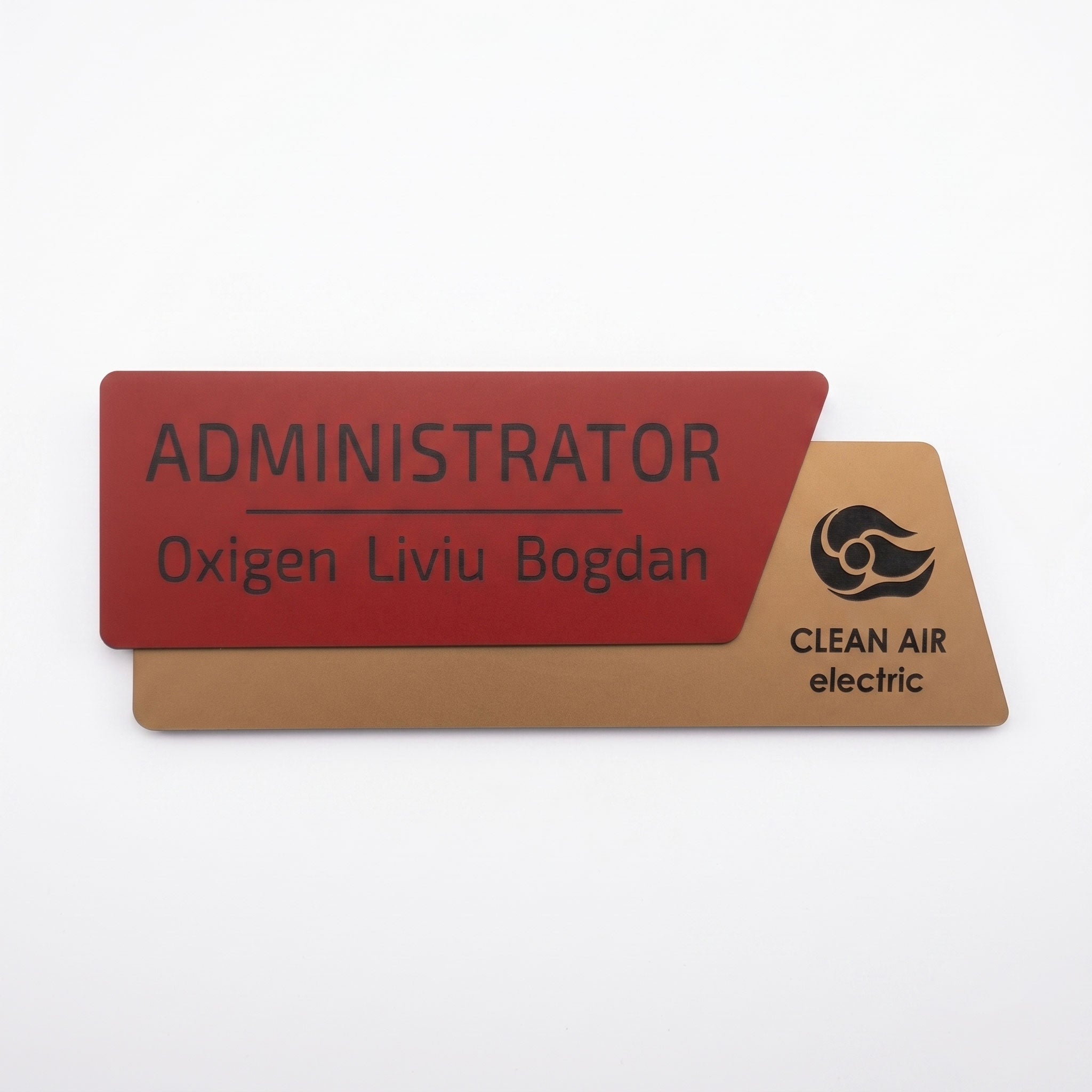 Plăcuță de identificare asimetrică pentru birou formată din două elemente, cu fața roșu închis mat gravată cu numele „ADMINISTRATOR Oxigen Liviu Bogdan” și o bază cu textură de lemn maro deschis cu logo-ul Clean Air electric, pe fundal alb.