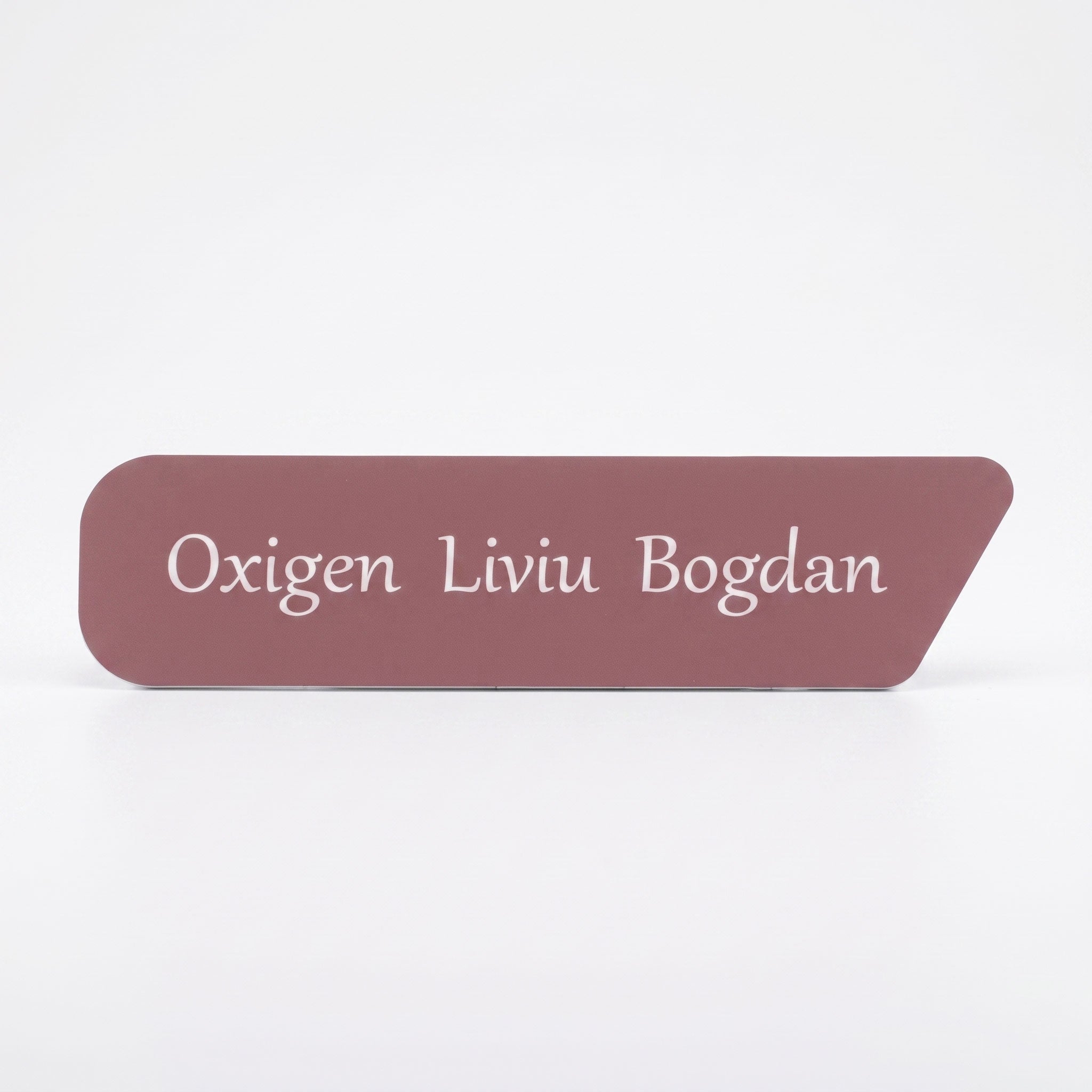 Placuta de identificare simpla pentru birou din acril roz prafuit mat, cu taietura asimetrica pe coltul din dreapta, gravata cu textul alb „Oxigen Liviu Bogdan”, pe fundal alb.
