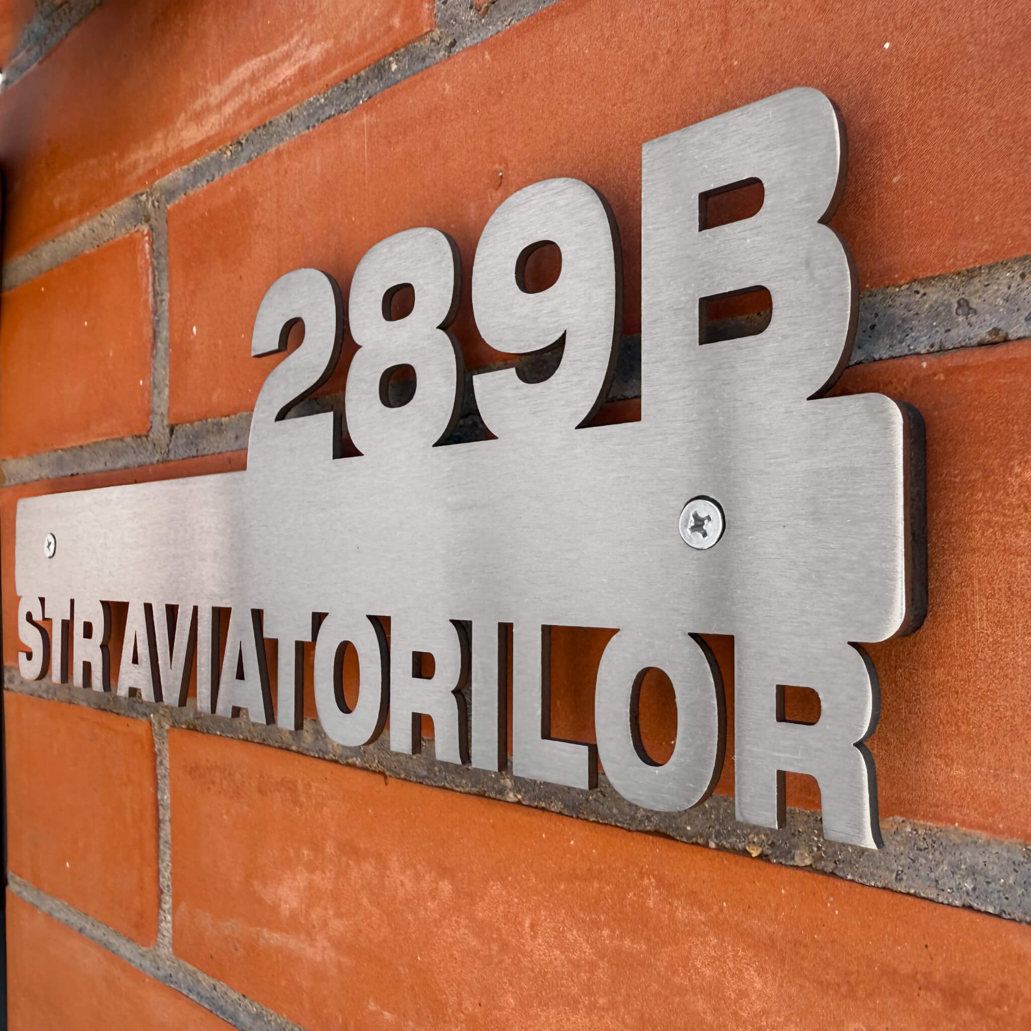 Vedere din unghi a numărului de casă din inox, evidențiind distanțierele care creează un elegant efect de umbră 3D pe perete.