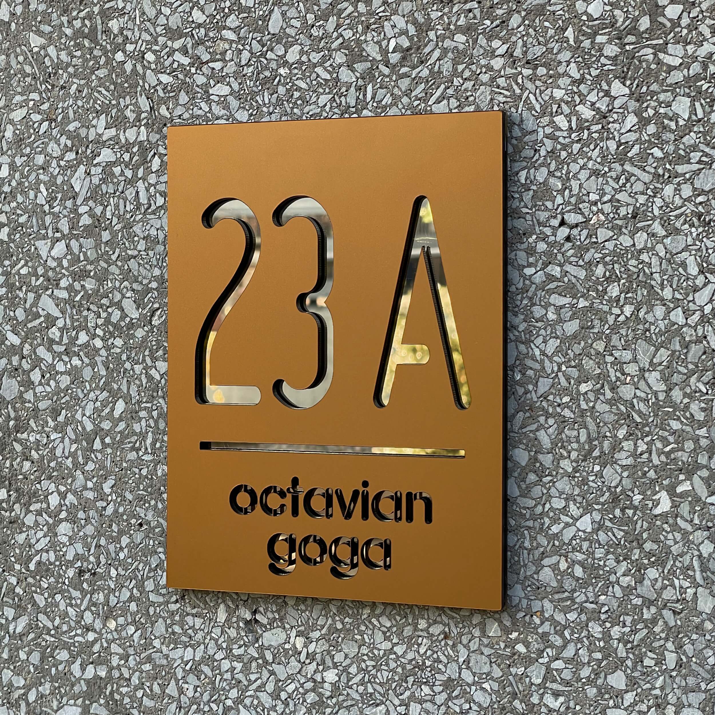 Prim plan cu numar de casa acrilic din bronz cu accent auriu oglinda pe perete pietruit