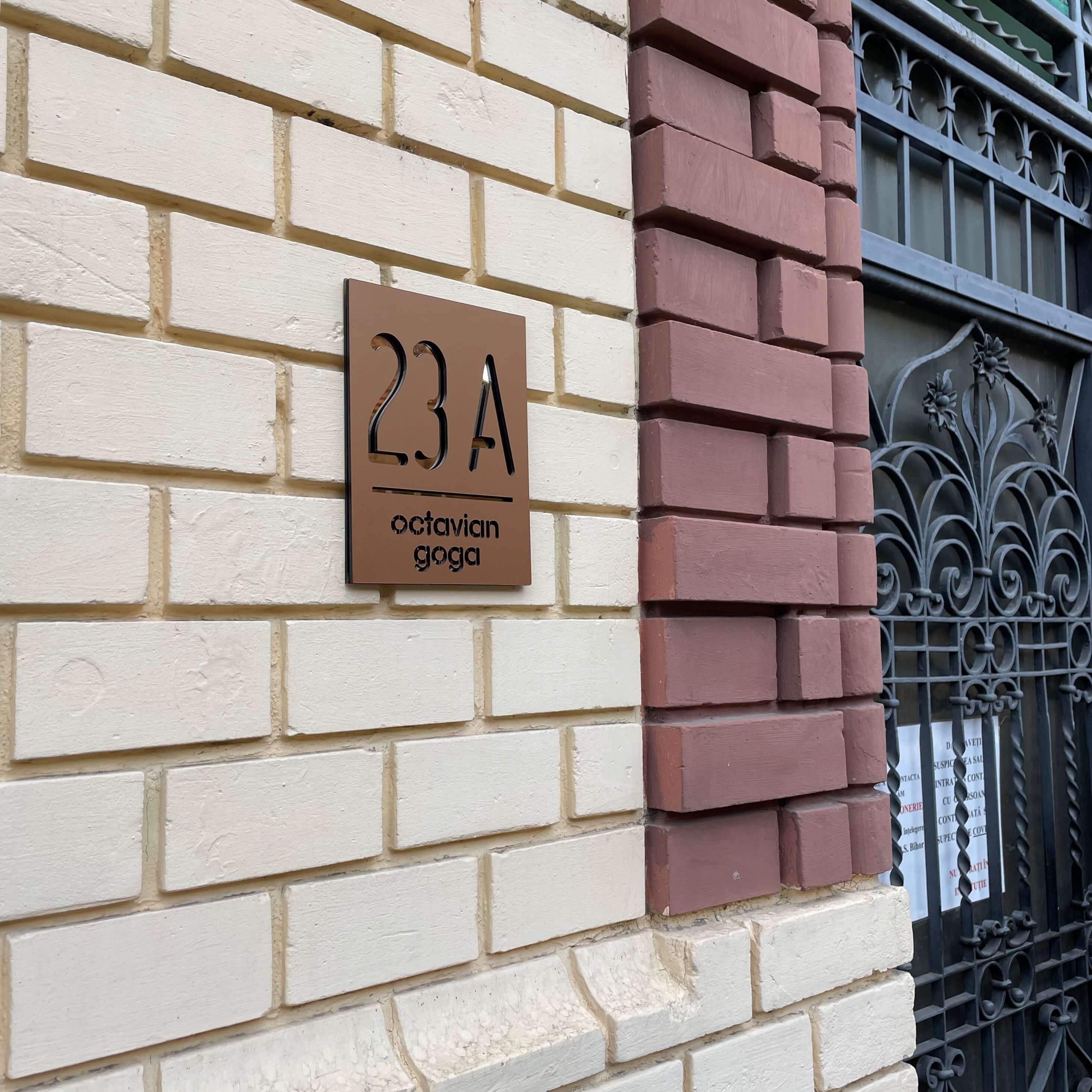 Placheta bronz cu accent auriu oglinda pe un perete de caramida din lateral