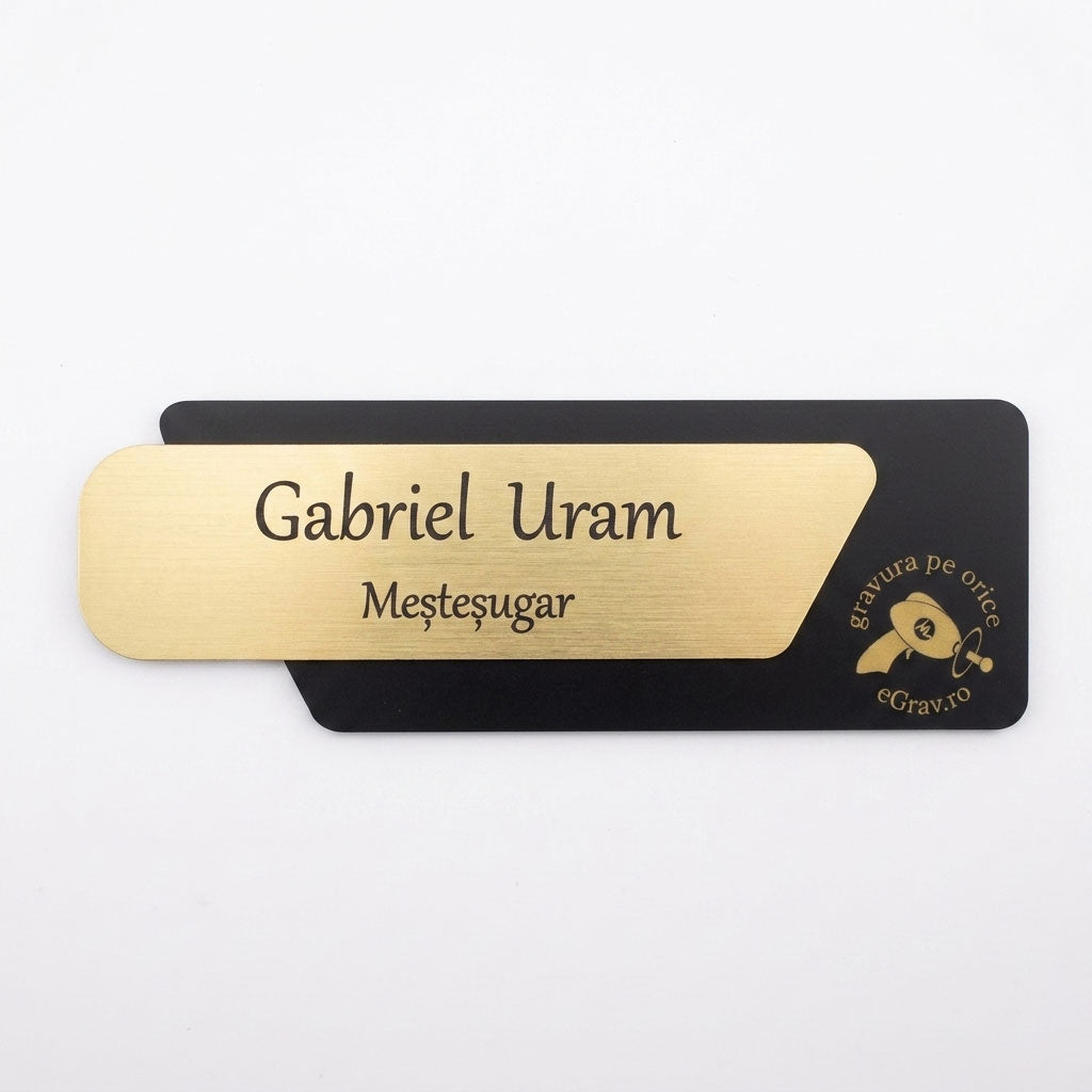 Plăcuță premium de identificare pentru birou formată din două elemente, cu fața metalică auriu periat gravată cu textul „Gabriel Uram Meșteșugar” și o bază asimetrică neagră mată cu logo-ul eGrav.ro, pe fundal alb.