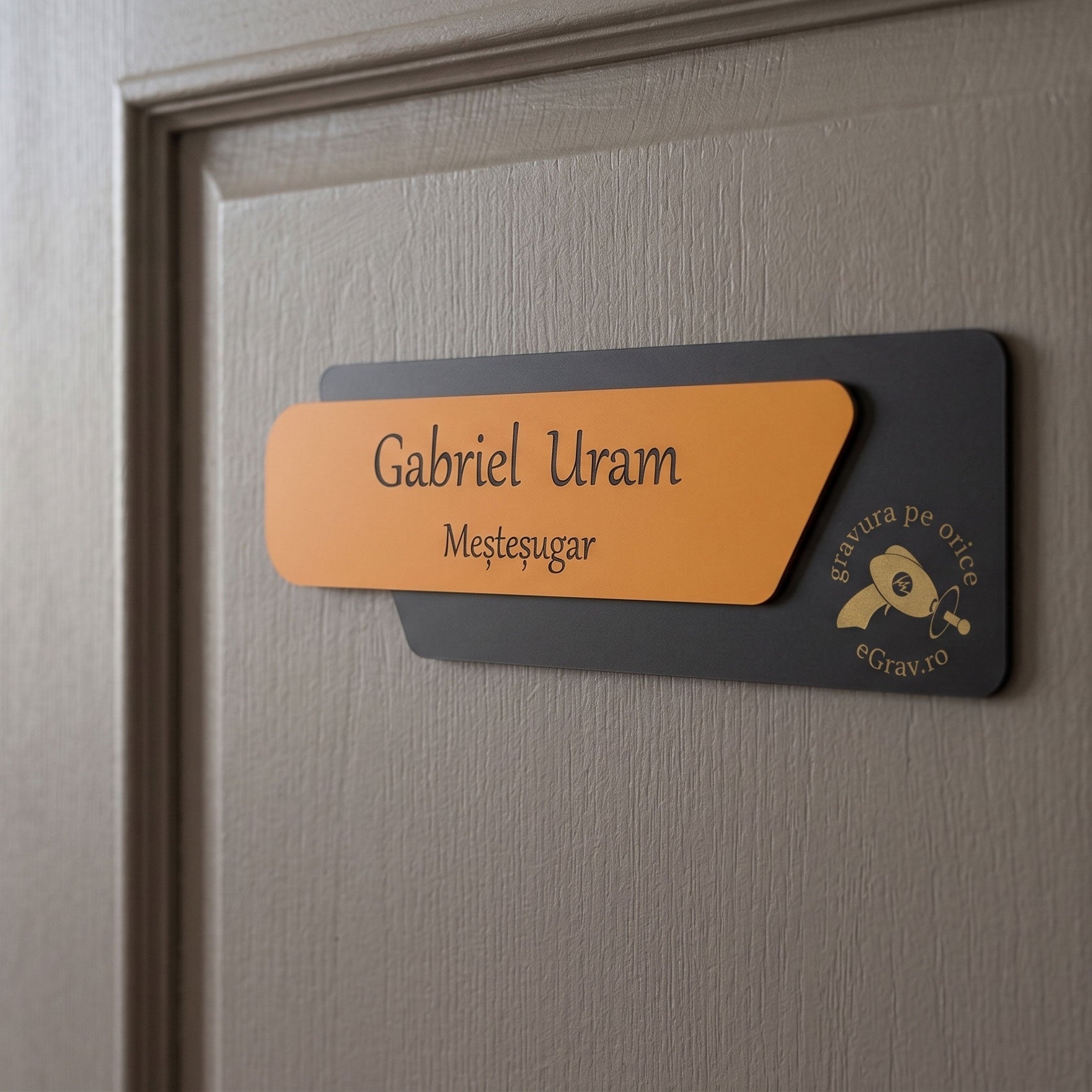 Plăcuță asimetrică completă pentru ușă de birou, varianta cu fața portocaliu mat și bază gri închis, montată pe o ușă din lemn texturat într-un decor modern de birou.
