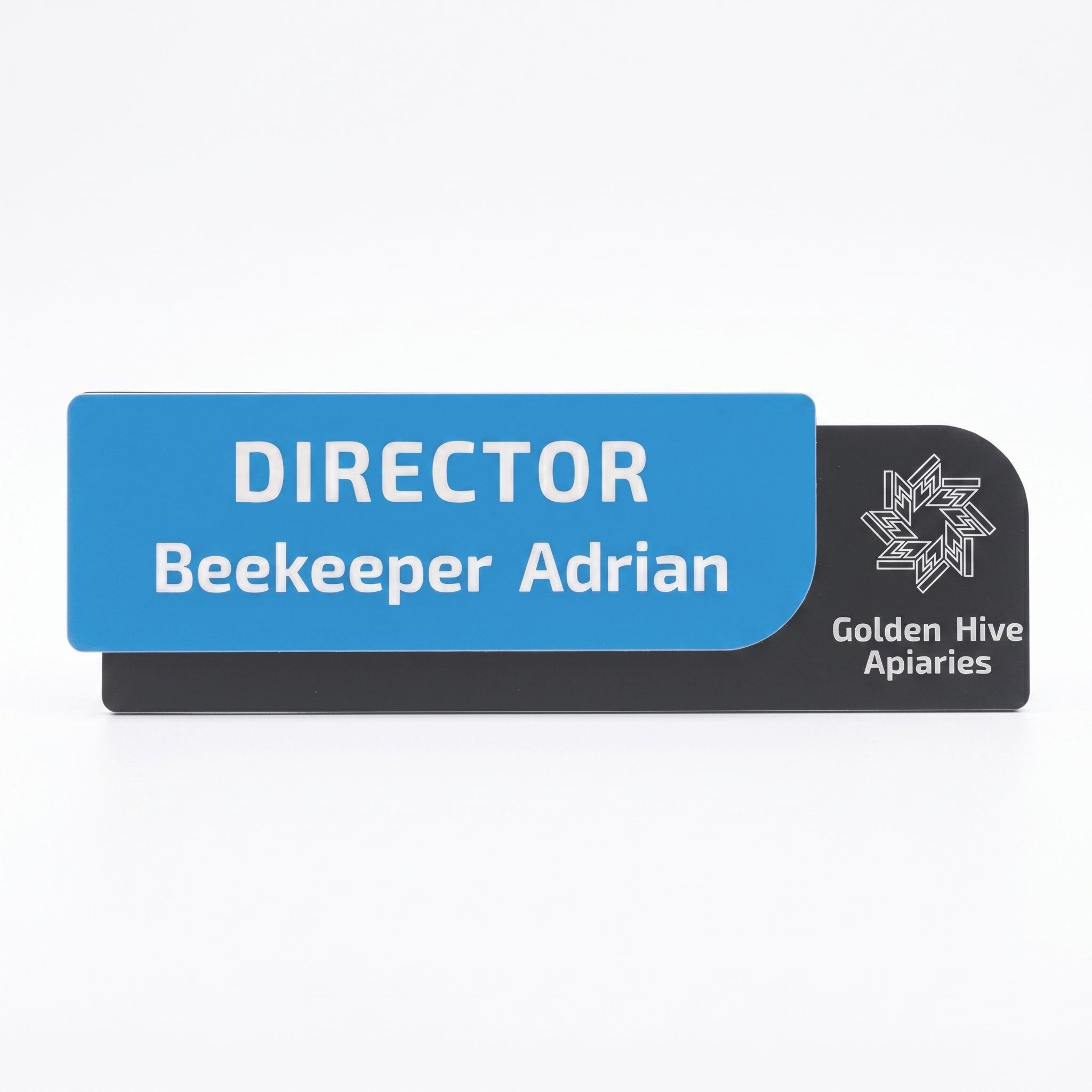 Plăcuță modernă de identificare pentru ușă de birou, formată dintr-un strat frontal albastru cu textul alb „DIRECTOR Beekeeper Adrian” și o bază neagră pe care este imprimat logo-ul și textul „Golden Hive Apiaries”, pe fundal alb curat.