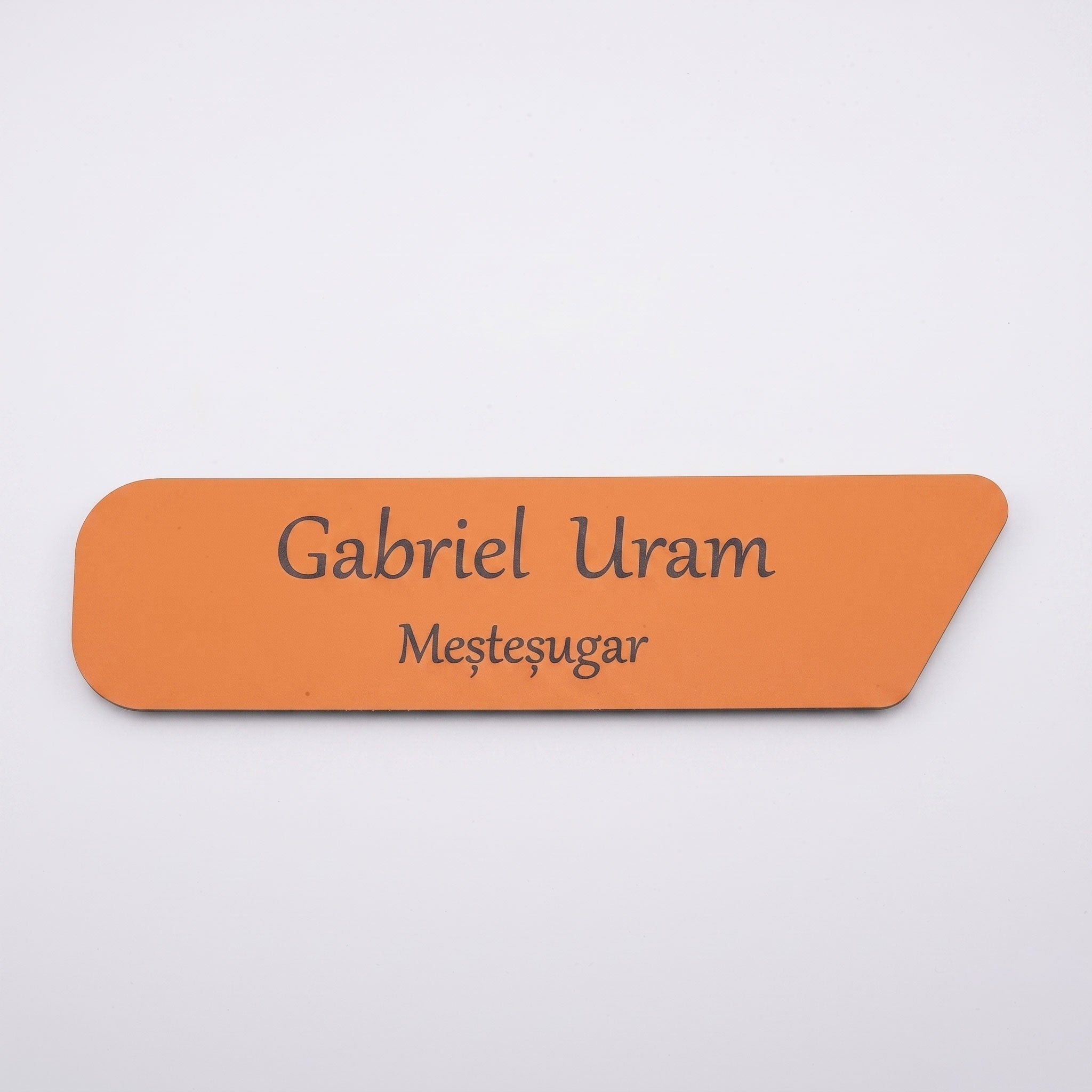 Plăcuță de identificare simplă pentru birou din acril portocaliu mat, cu tăietură asimetrică pe colțul din dreapta, gravată cu textul „Gabriel Uram Meșteșugar”, pe fundal alb.