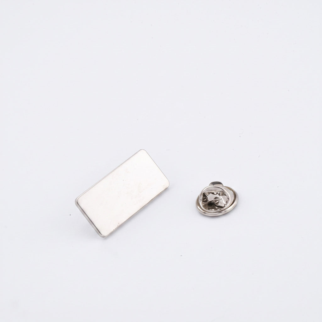 Insigna metalica personalizabila din gama silver cu forma dreptunghiulara si dimensiune de 2.5x1.2 cm, dotata cu ac de siguranta si clema fluture argintie.